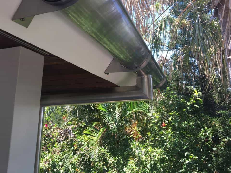 A Gutter on the Side of a Building With Trees in the Background — Reed Plumbing Industries in Mackay, QLD