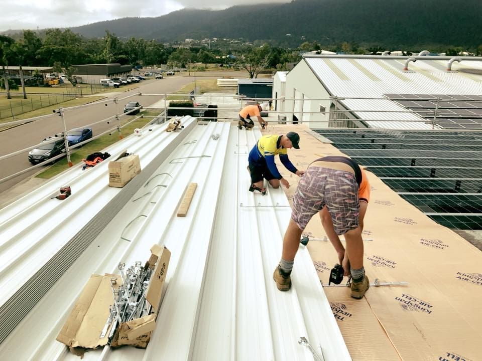 A Group of People Are Working on the Roof of a Building — Reed Plumbing Industries in Airlie Beach, QLD