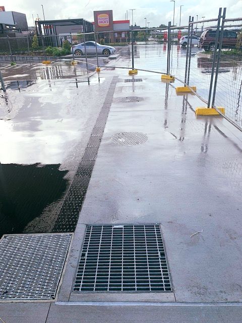 A Metal Grate is on the Sidewalk Next to a Puddle of Water — Reed Plumbing Industries in Mackay, QLD