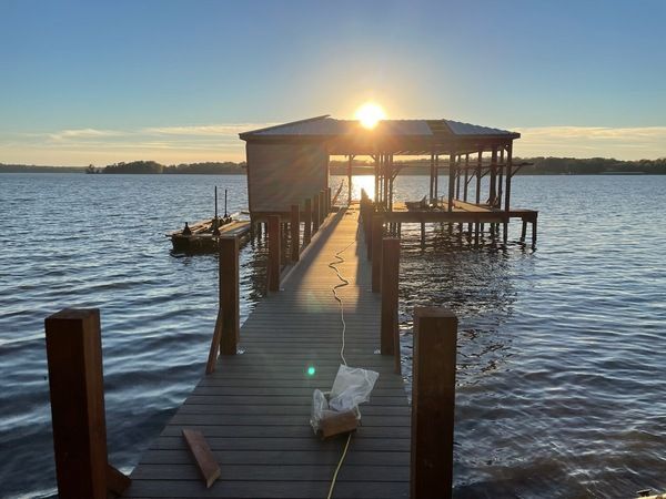 The sun is setting over a dock in the middle of a lake.