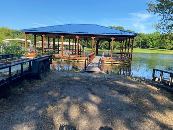 A gazebo is sitting on the shore of a lake next to a trailer.