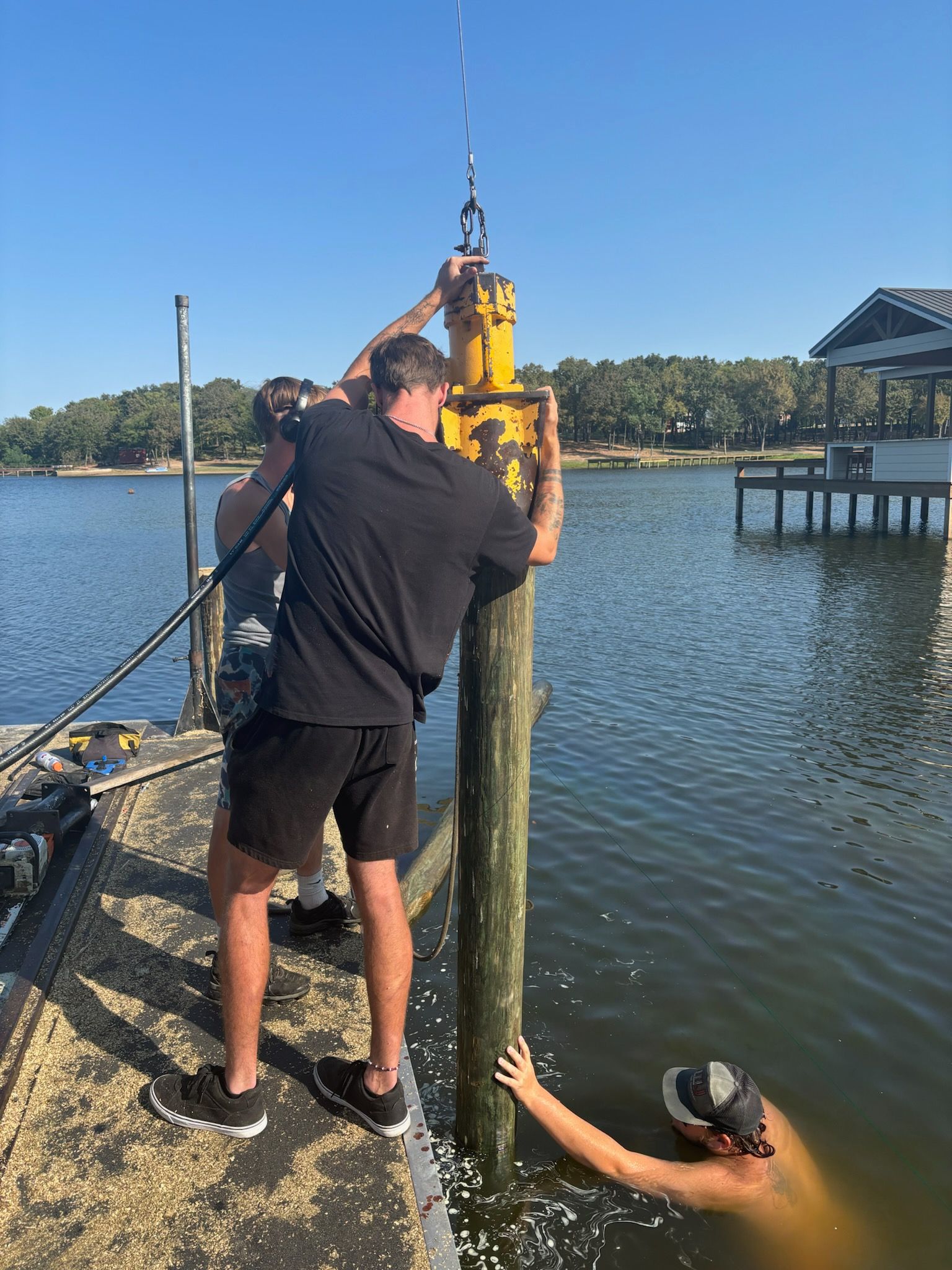 Two men are working on a wooden post in the water.