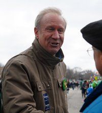 A man in a brown jacket is talking to another man in a black hat.