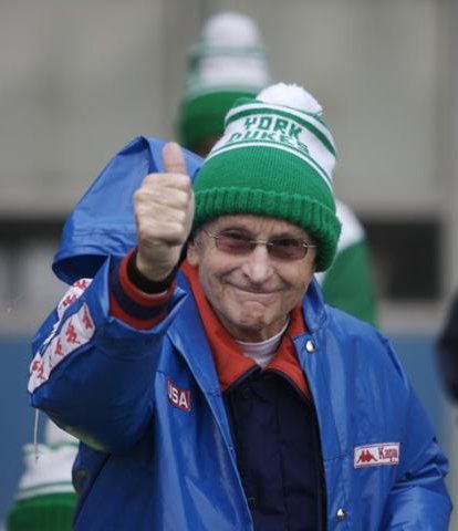 A man wearing a blue jacket and a green hat with the word york on it gives a thumbs up