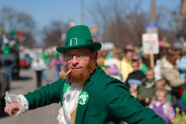 A man in a leprechaun costume is holding a pipe in his mouth.
