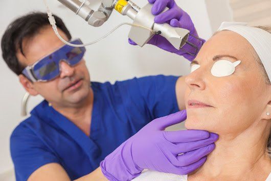 A person receiving laser skin treatment on their face and neck by a professional.