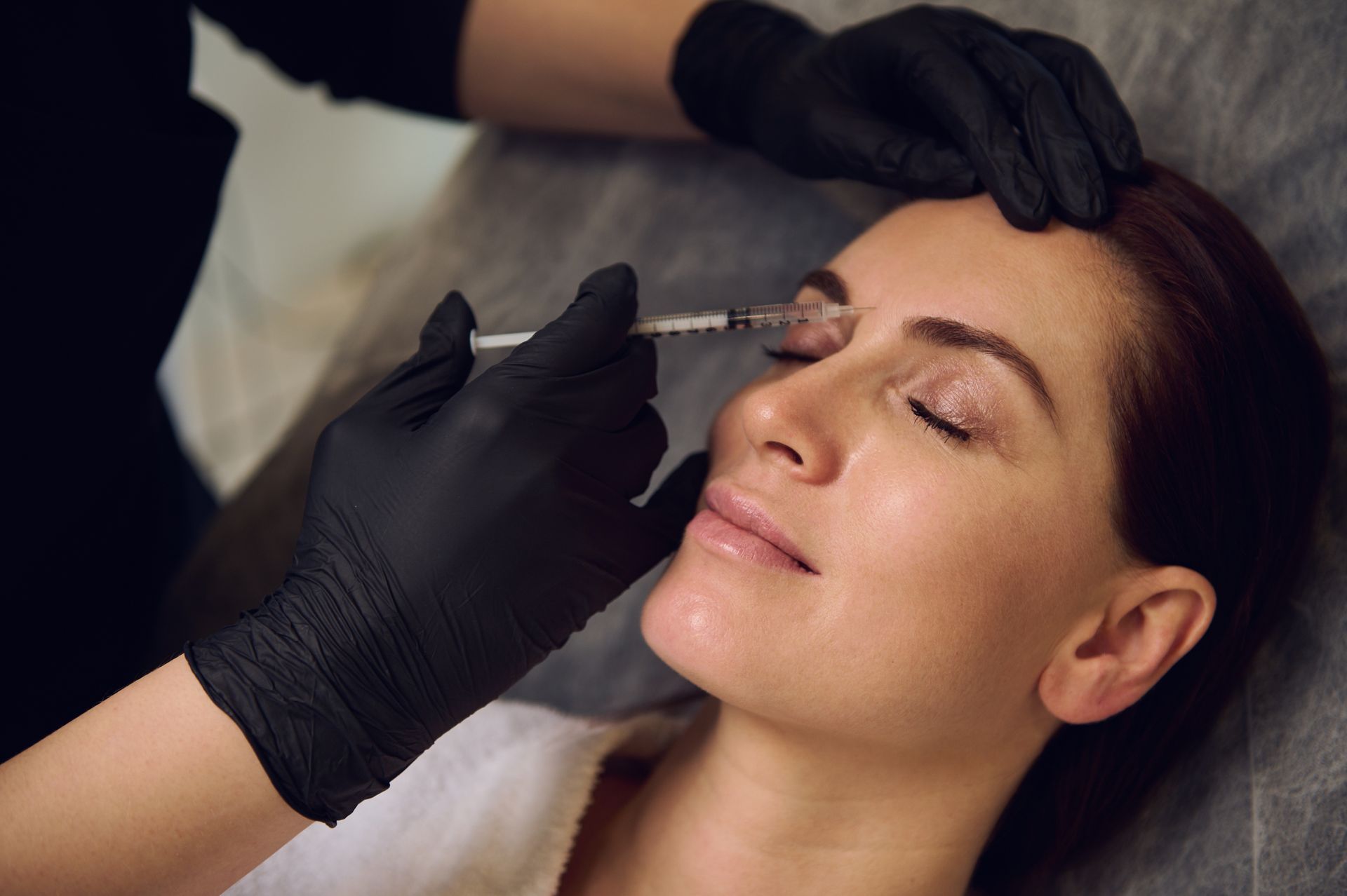 Middle-aged woman receiving forehead beauty injections at a spa clinic.