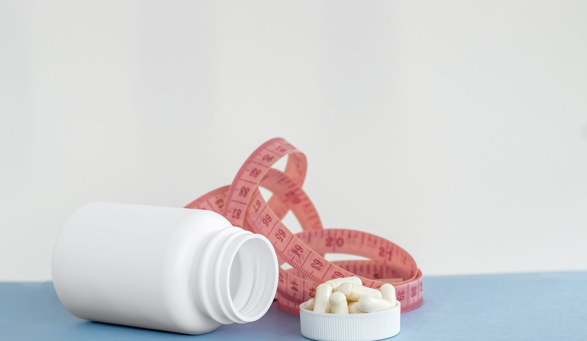 Photograph showing a white pill bottle lying on its side with capsules spilled onto its white cap, 