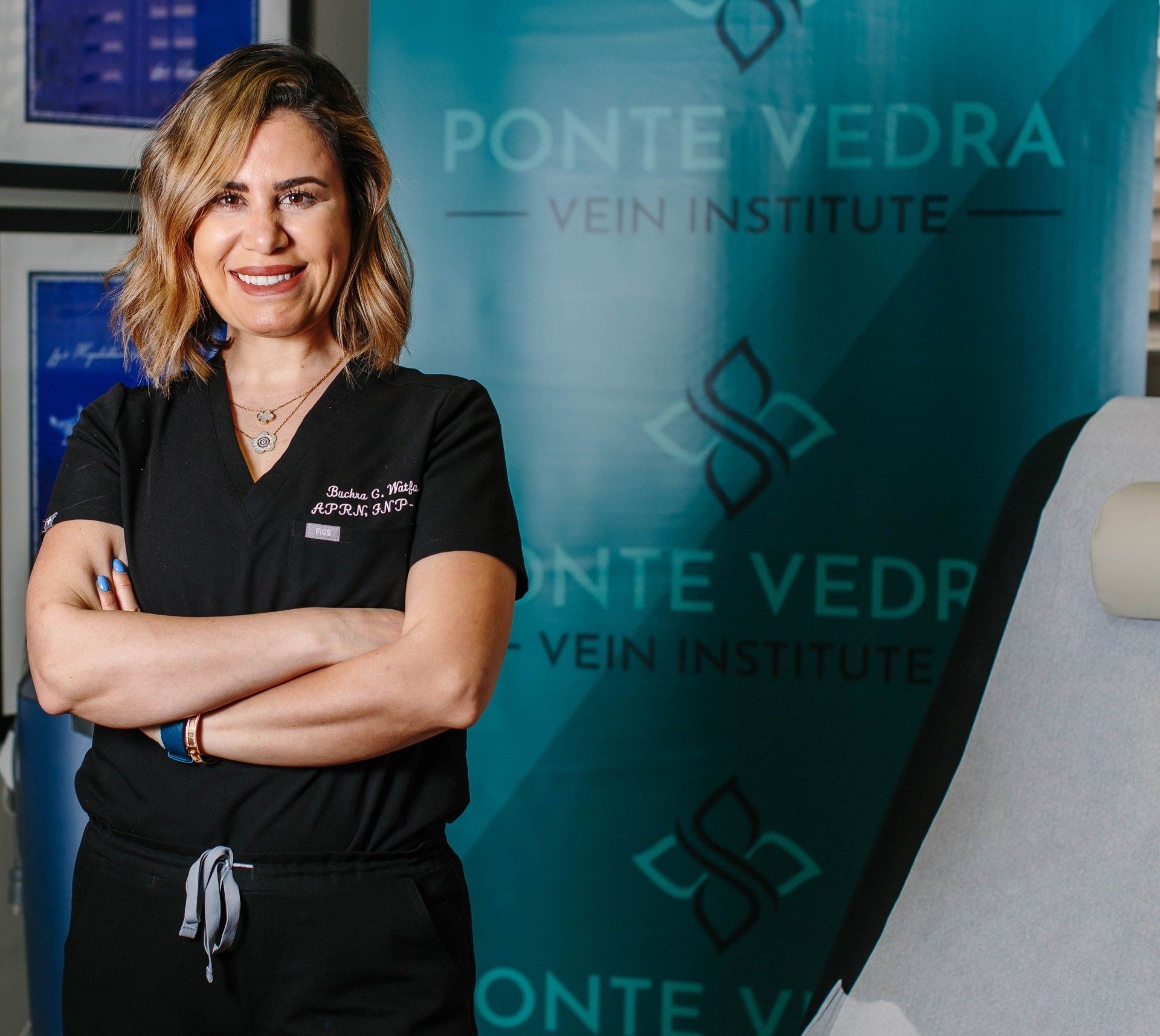 Woman in scrubs with arms crossed, in front of a Ponte Vedra Vein & Aesthetics banner.