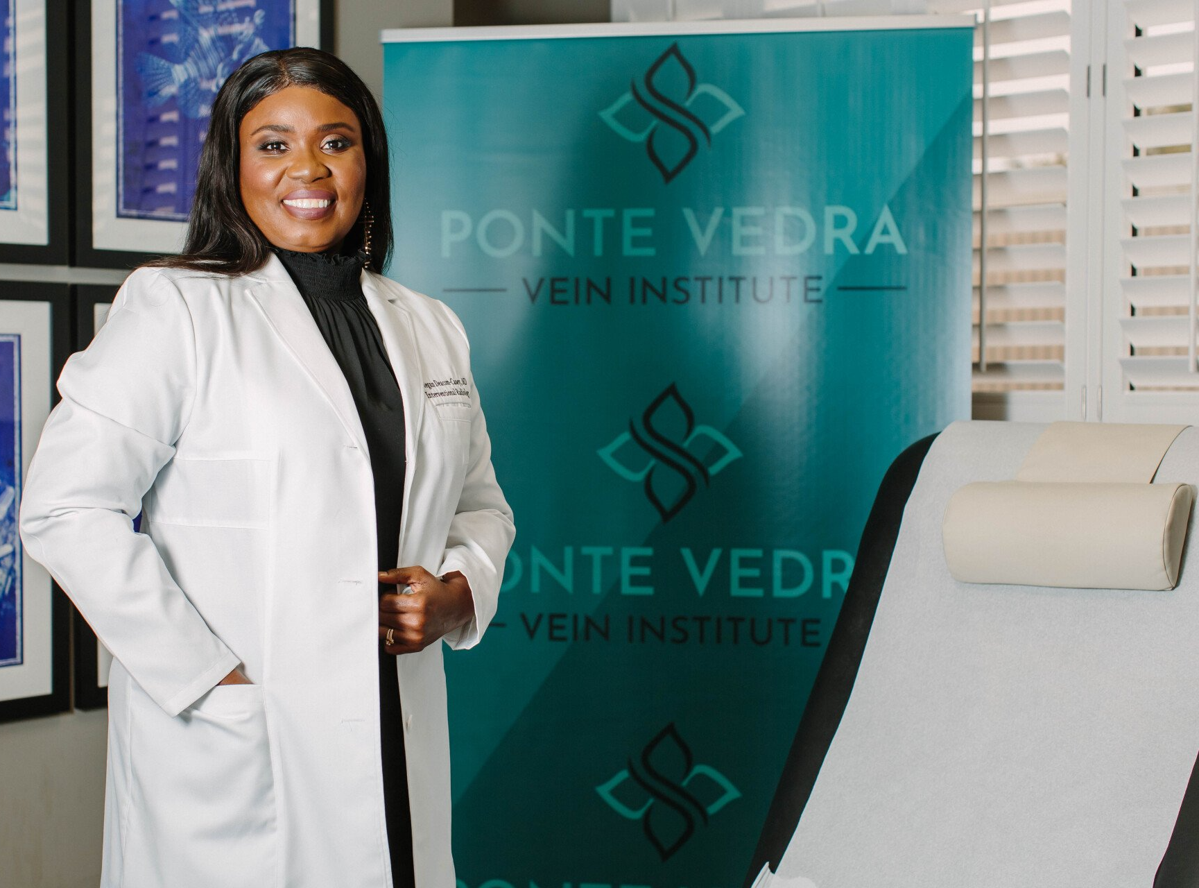 Woman in lab coat stands in a medical office, Ponte Vedra Vein & Aesthetics banner in background.