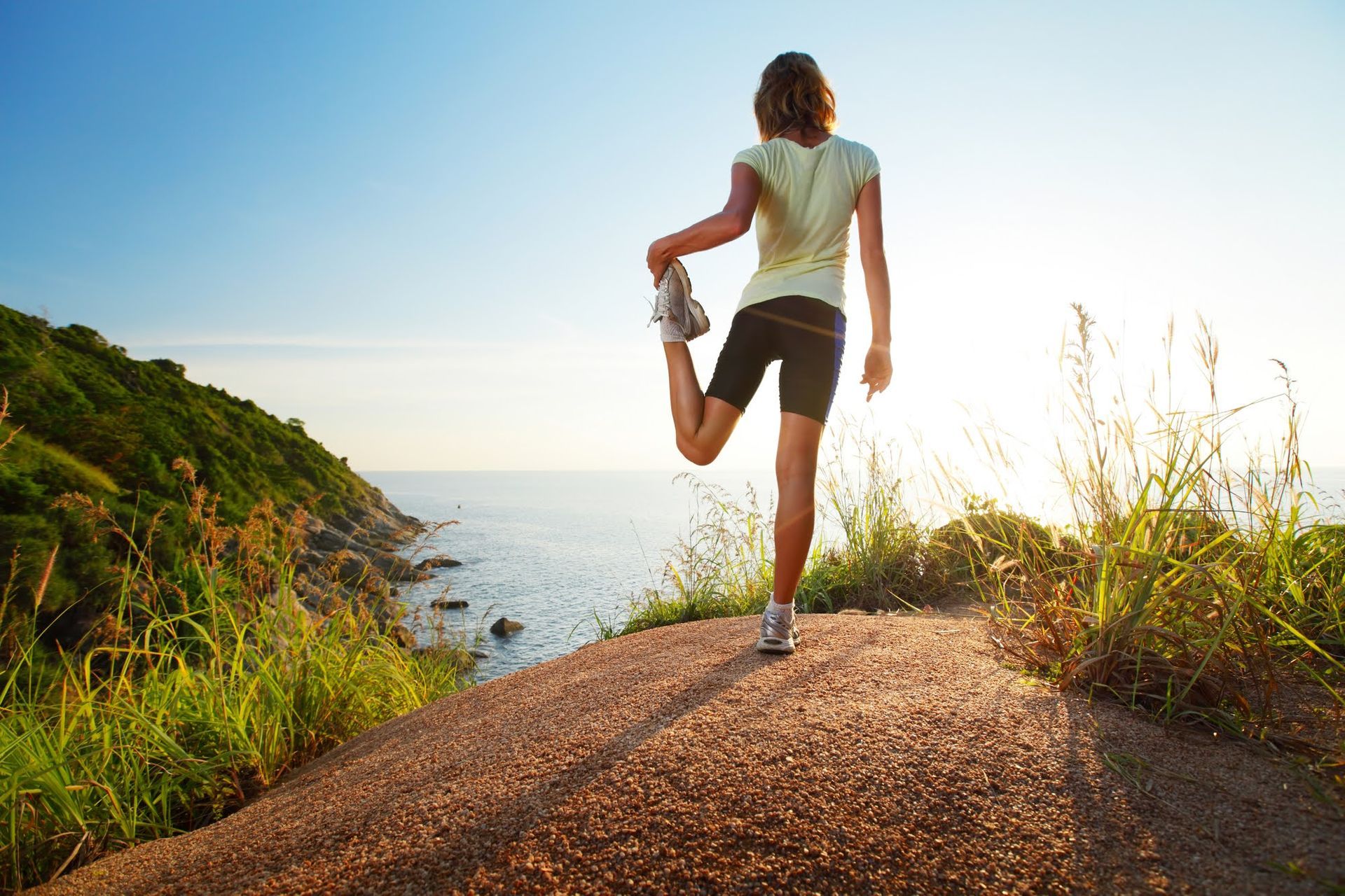 Woman stretching leg, ocean and green hills in background.