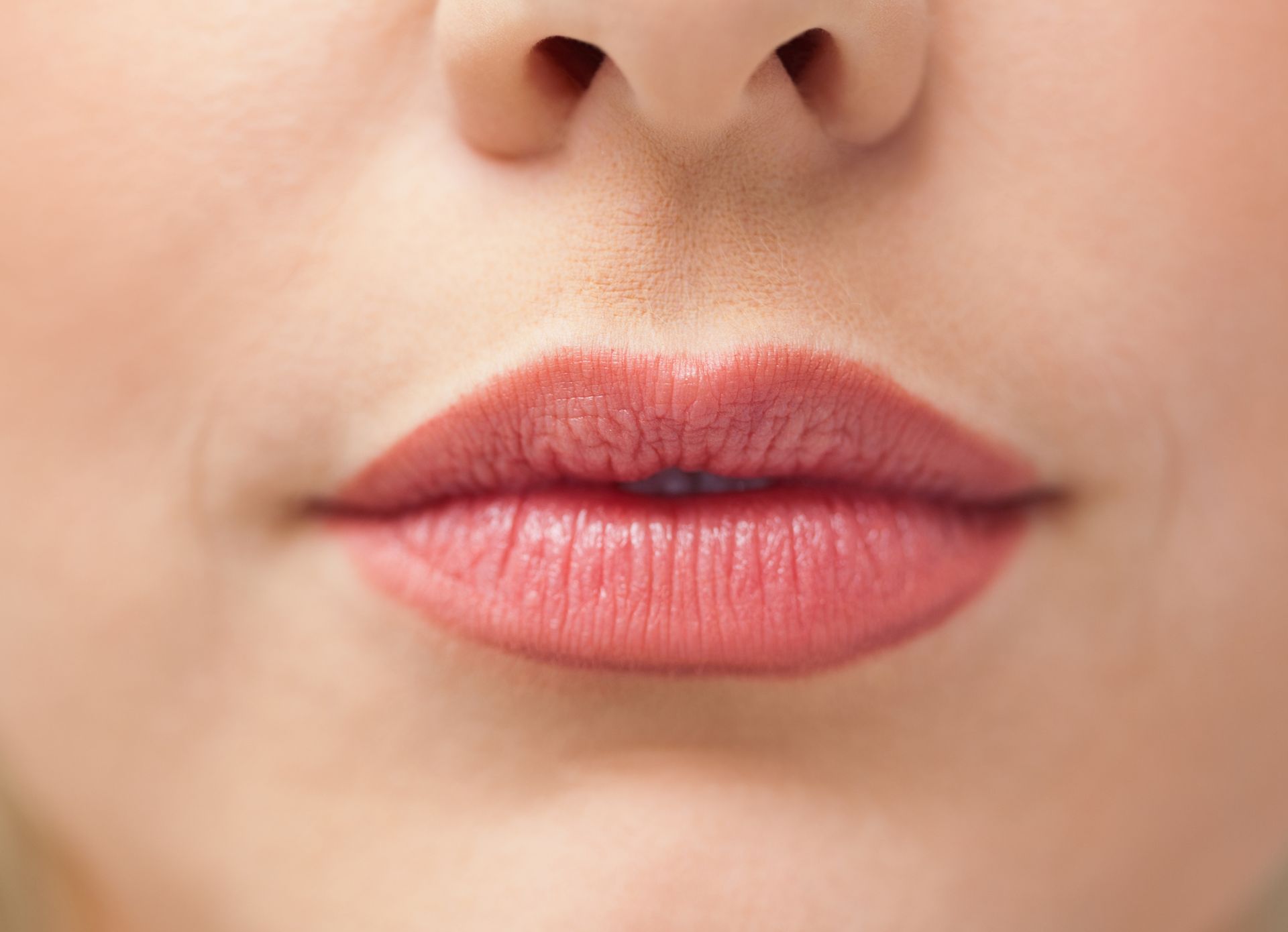 Close-up of a person's lips. The lips are full, colored with a nude shade of lipstick.
