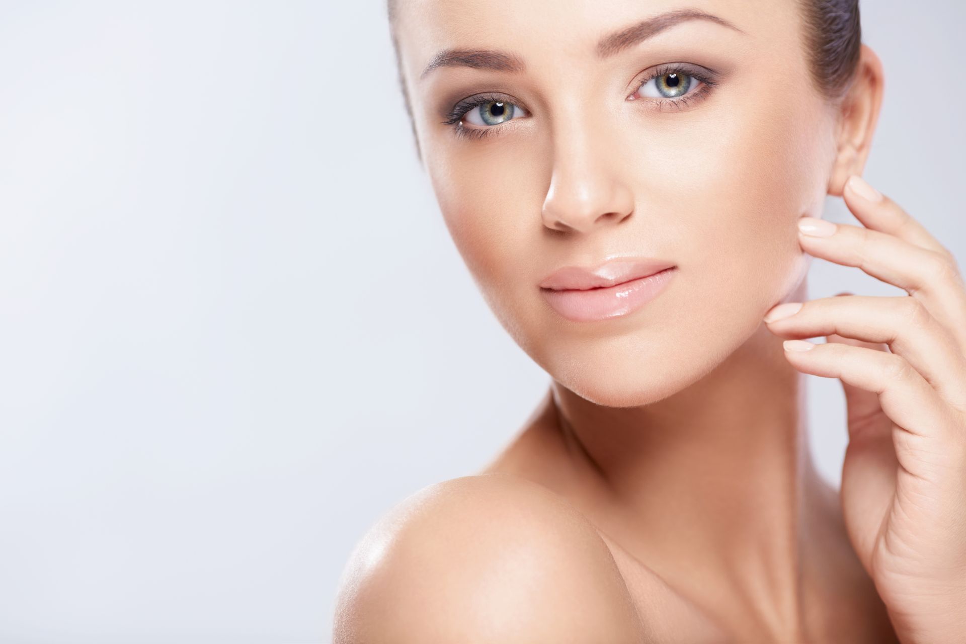 Woman with fair skin and brown eyeshadow touching her cheek, looking towards the camera.