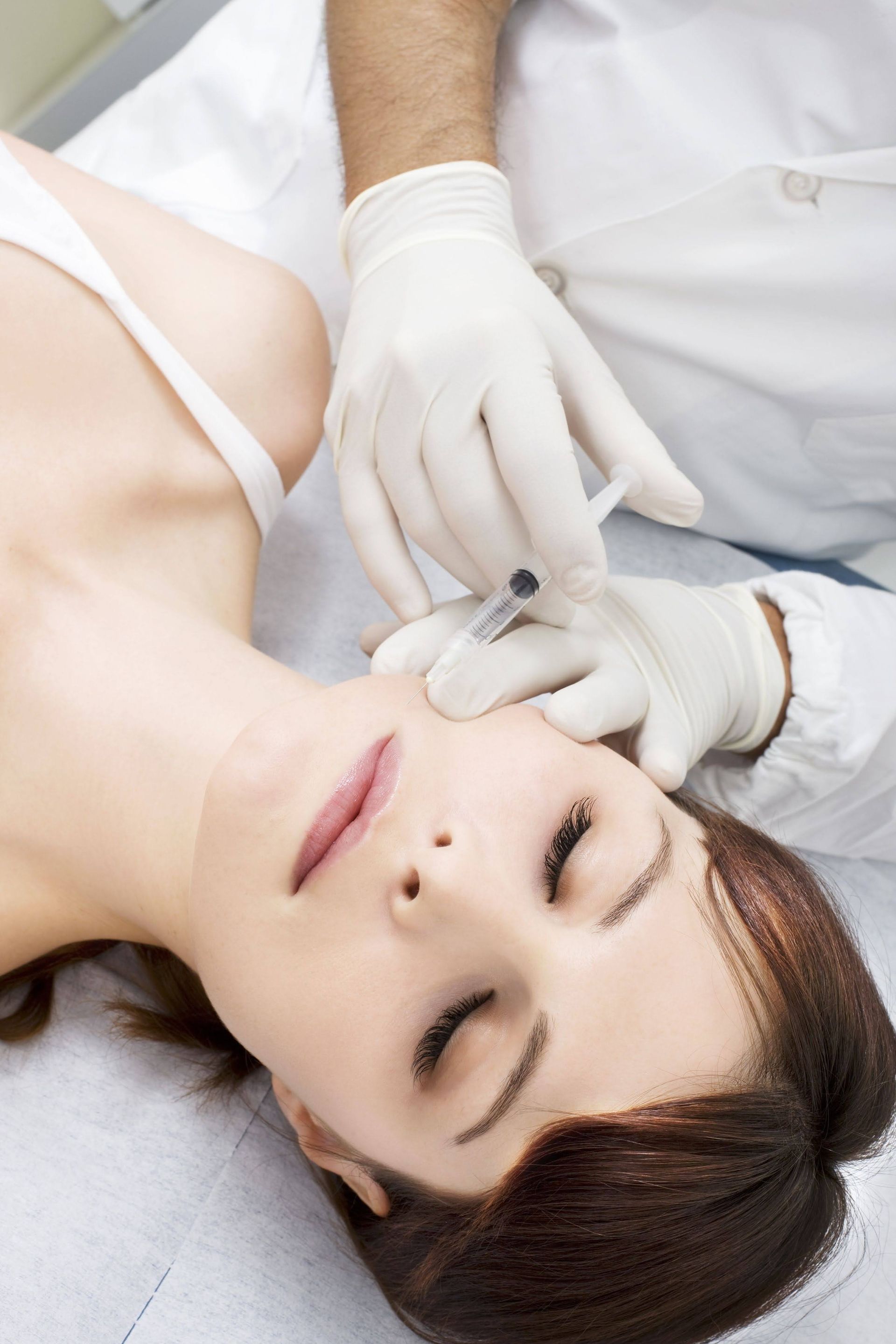 Person receiving a facial injection from someone wearing gloves and a white coat.