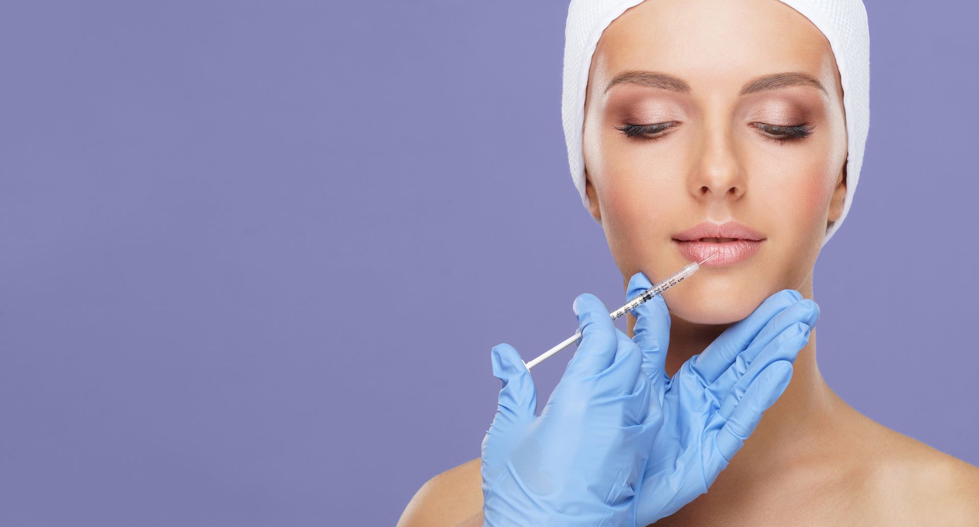 Person receiving lip filler injection with a syringe, blue gloves, purple background.