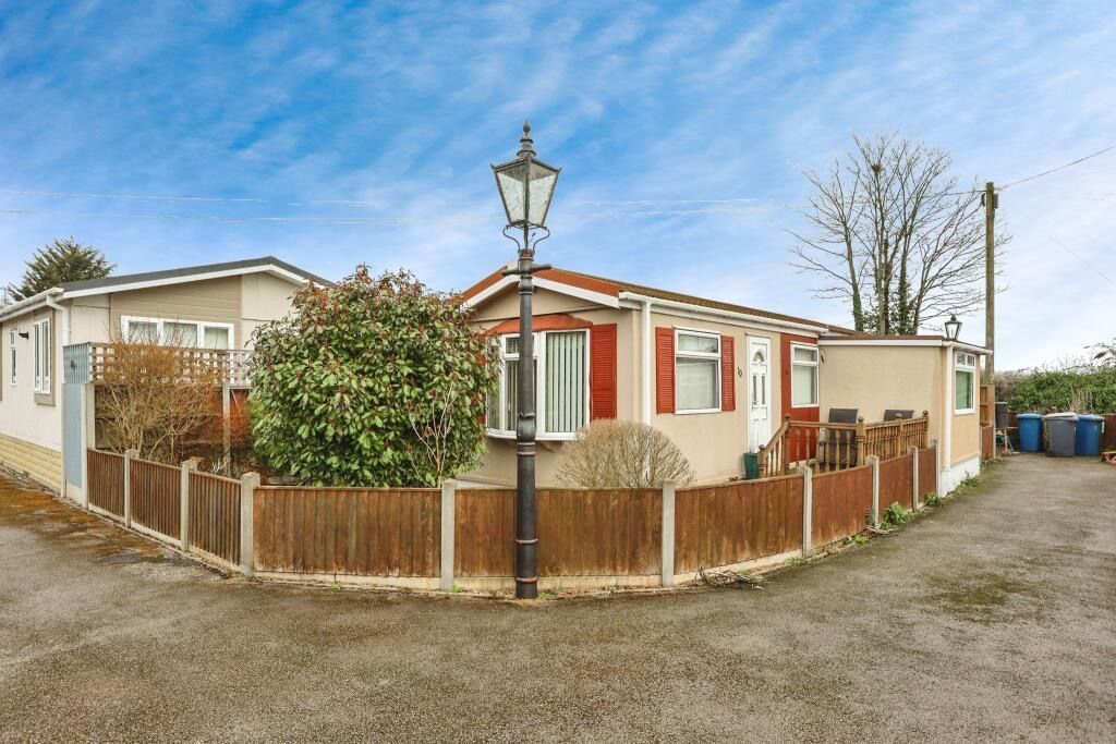 Mobile home with beige siding, red shutters, and a brown fence. A lamppost stands in front.