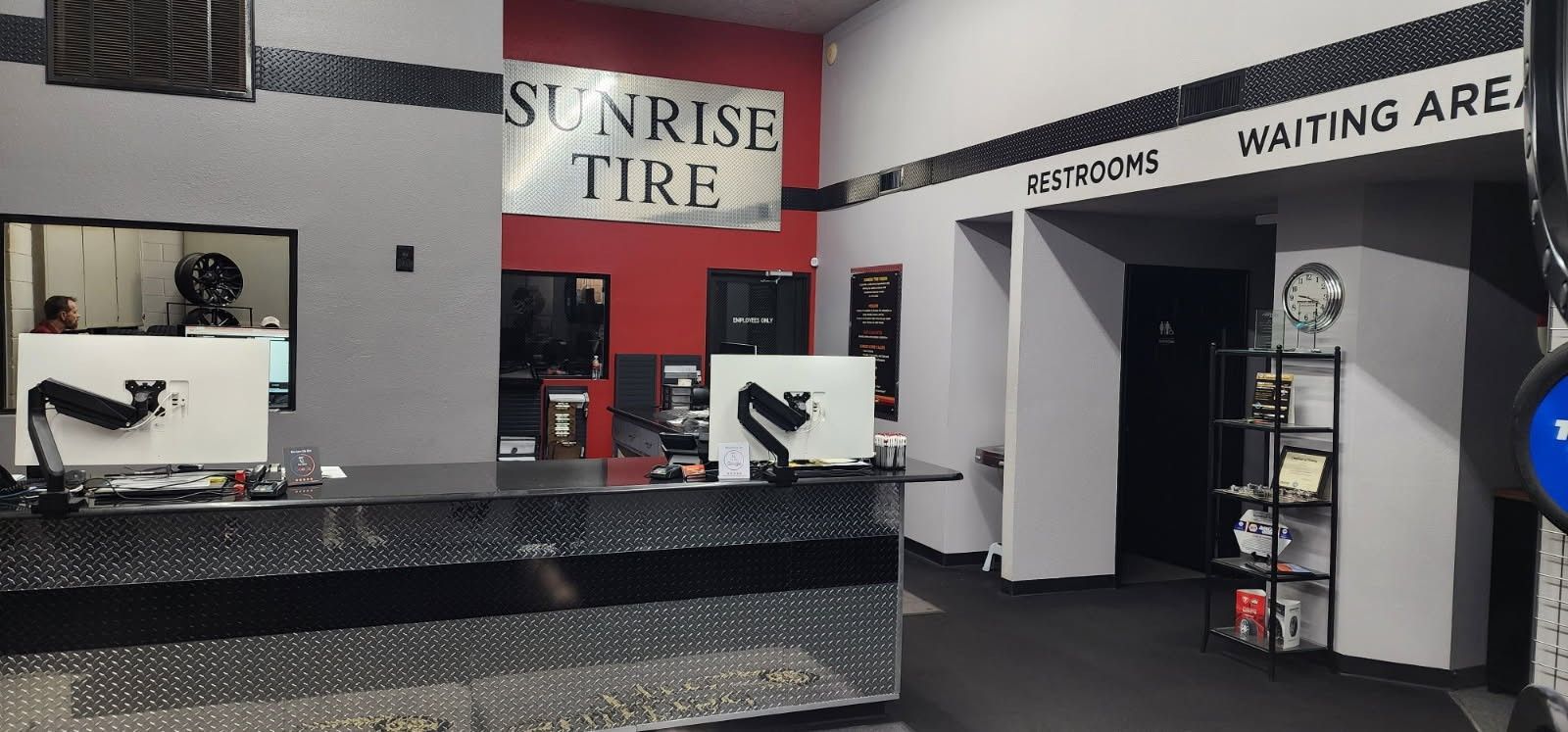 Auto service counter with gray walls, red accent banners, and a “waiting area” entrance