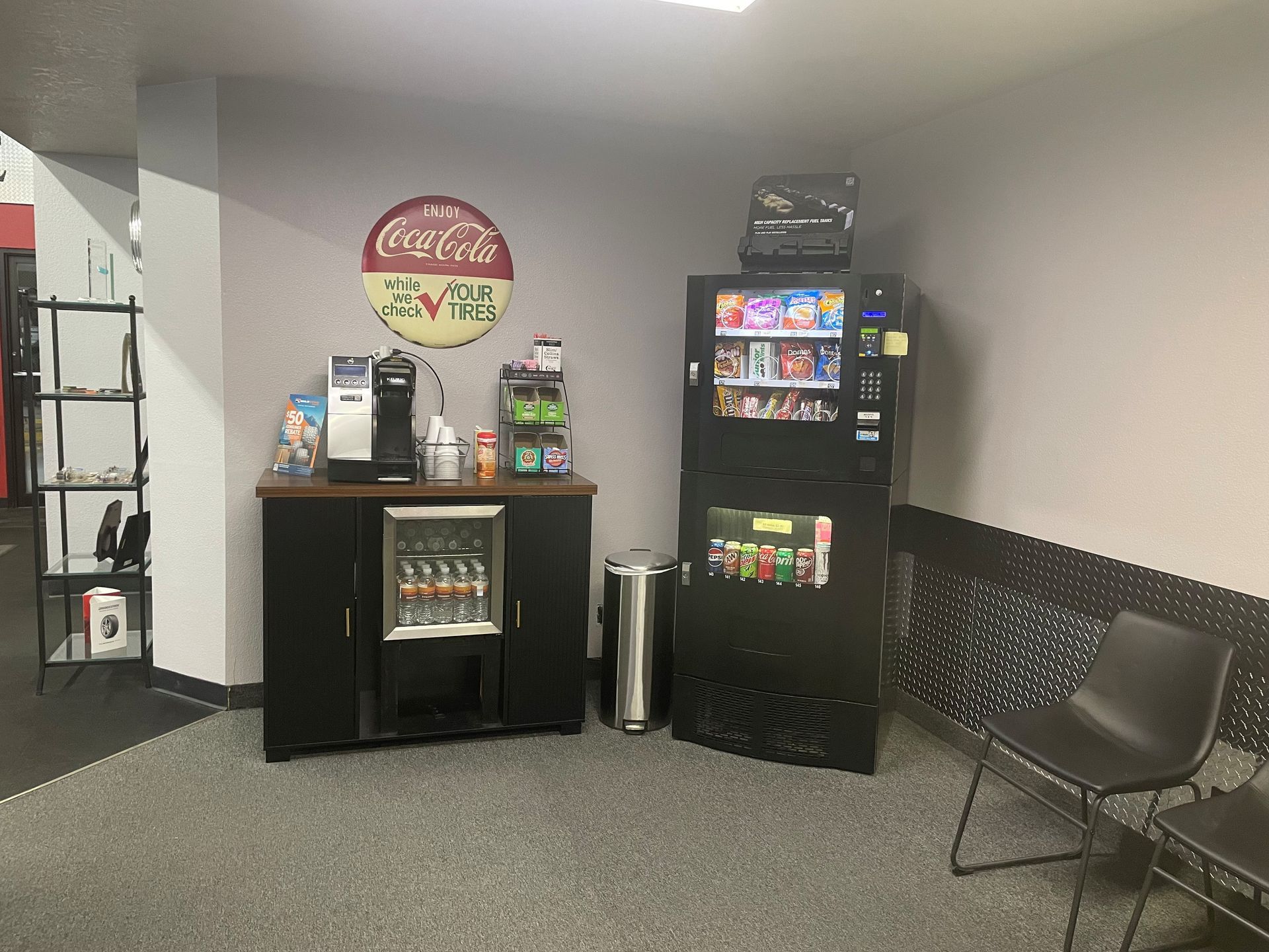 Office break room with Coca-Cola decor, vending machines, mini fridge, and a gray chair along the wall.