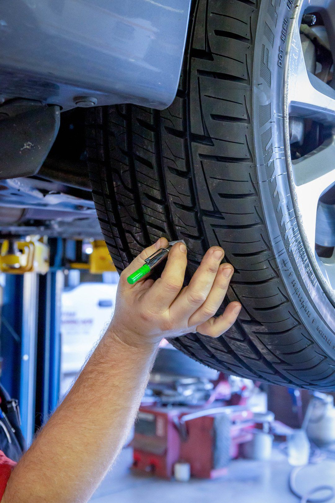 Mechanic inspecting a car tire with a green tool in an auto repair shop