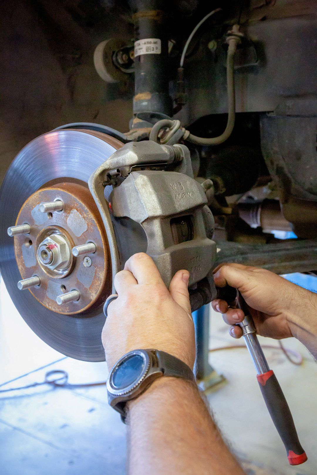 Mechanic removing a car brake caliper beside a rusty brake rotor in a garage