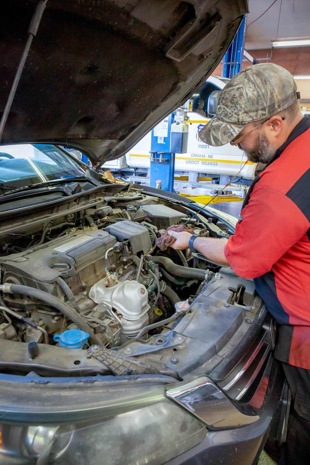 Mechanic in red jacket inspecting car engine under open hood in an auto shop
