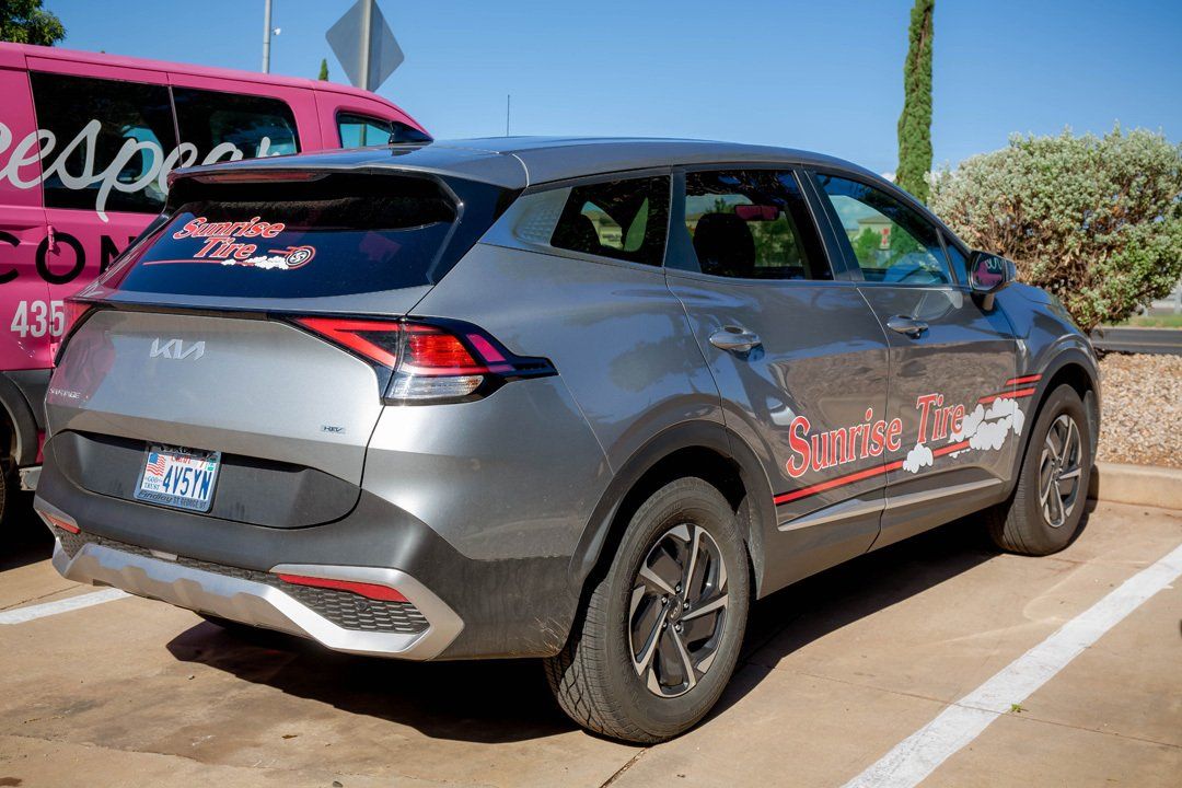 Gray SUV with red graphics parked outdoors beside a pink vehicle on a sunny day