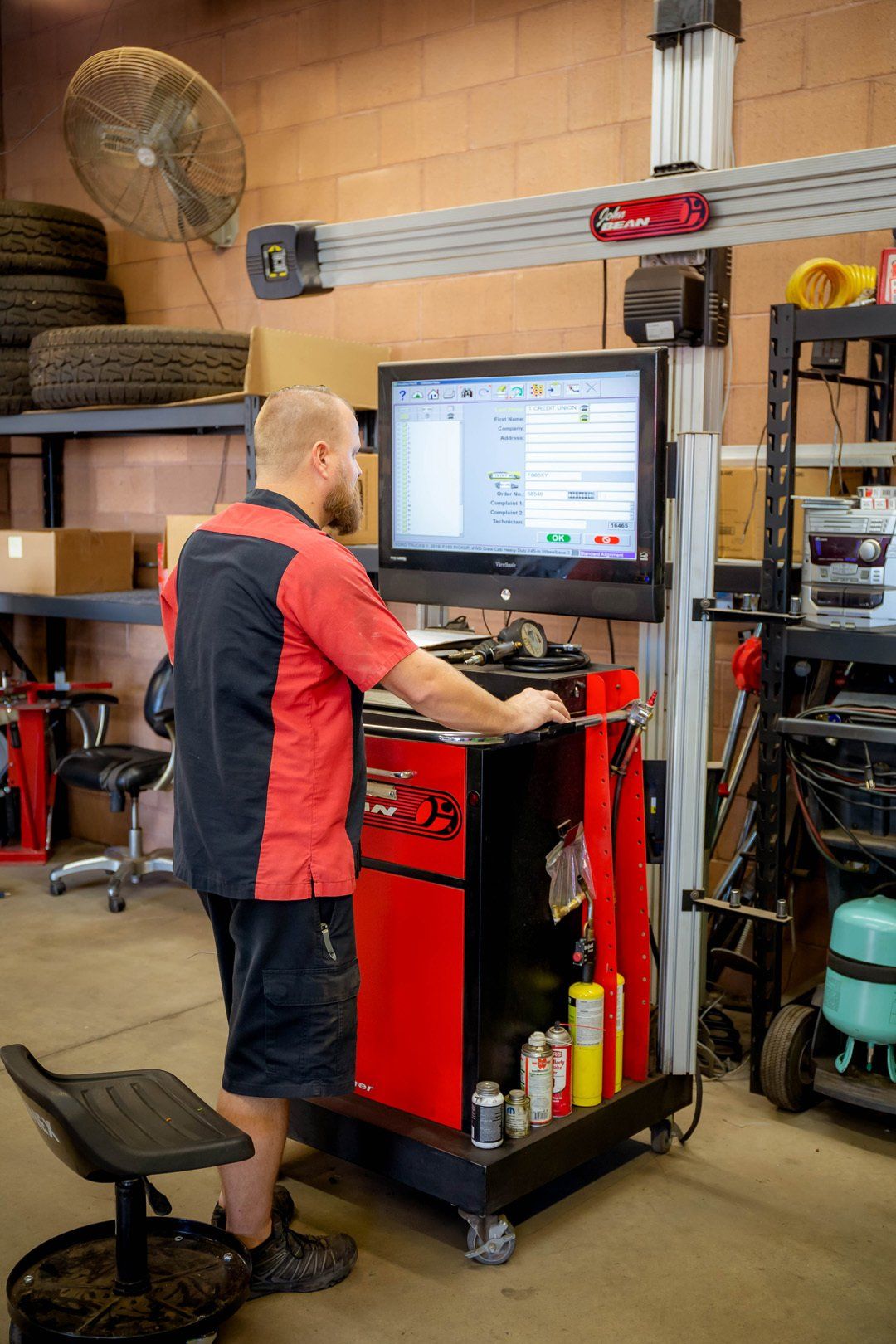 Mechanic using a red tire-changing machine in a workshop, with shelves and tools nearby