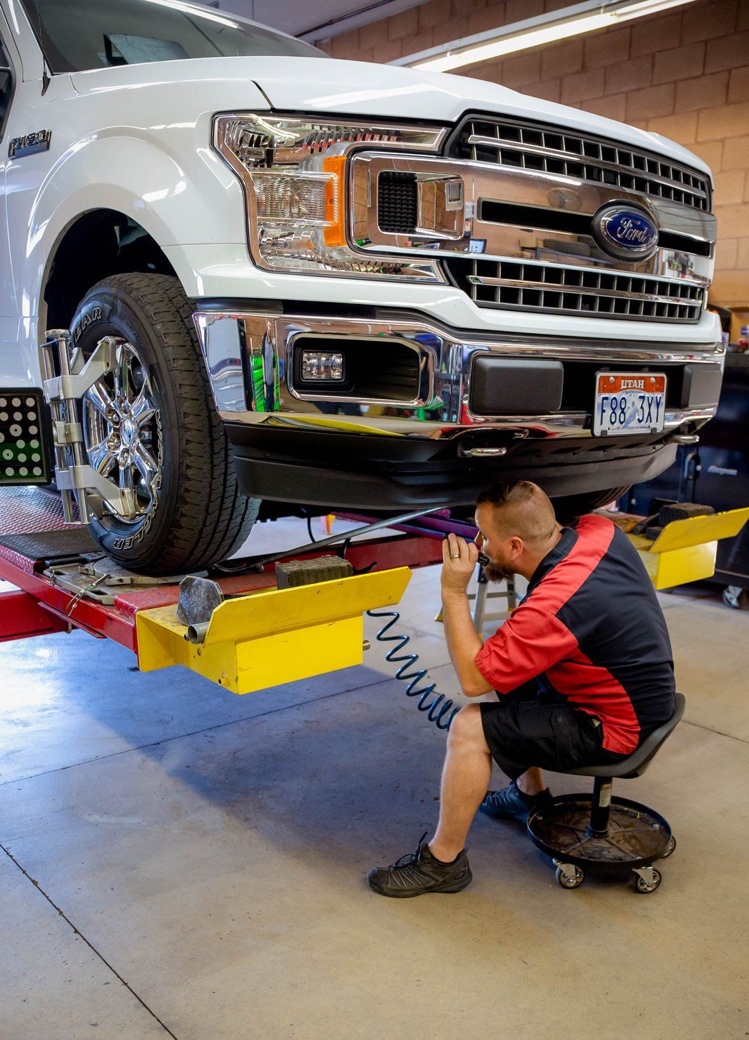 Mechanic working under a white pickup truck on a lift in a garage