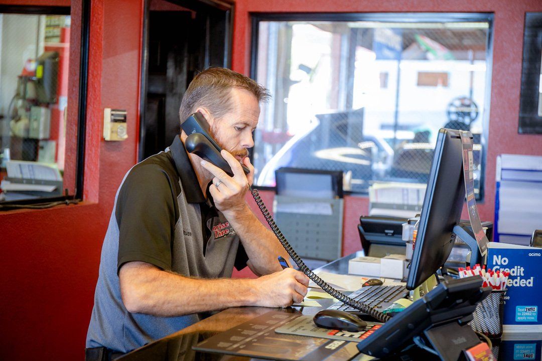 Man talking on a phone at a counter in a red-walled shop, with a computer and papers nearby