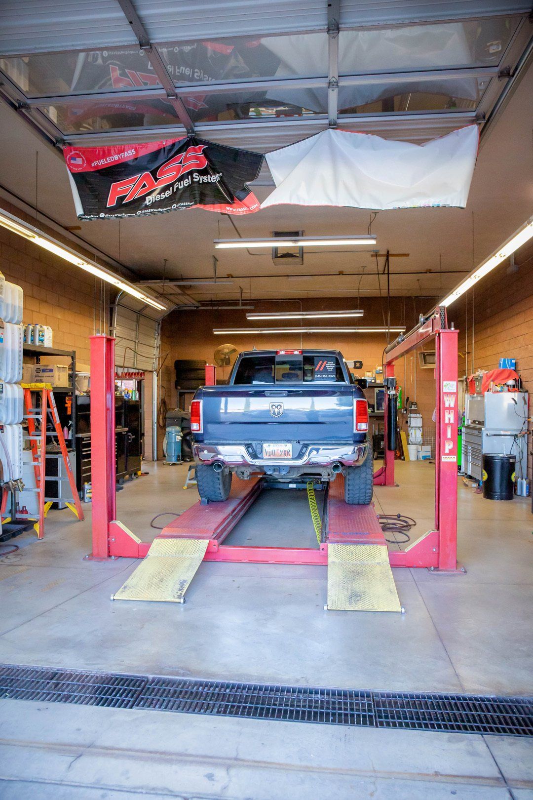 Blue pickup truck on lifts inside an auto repair garage with tools and open bay doors