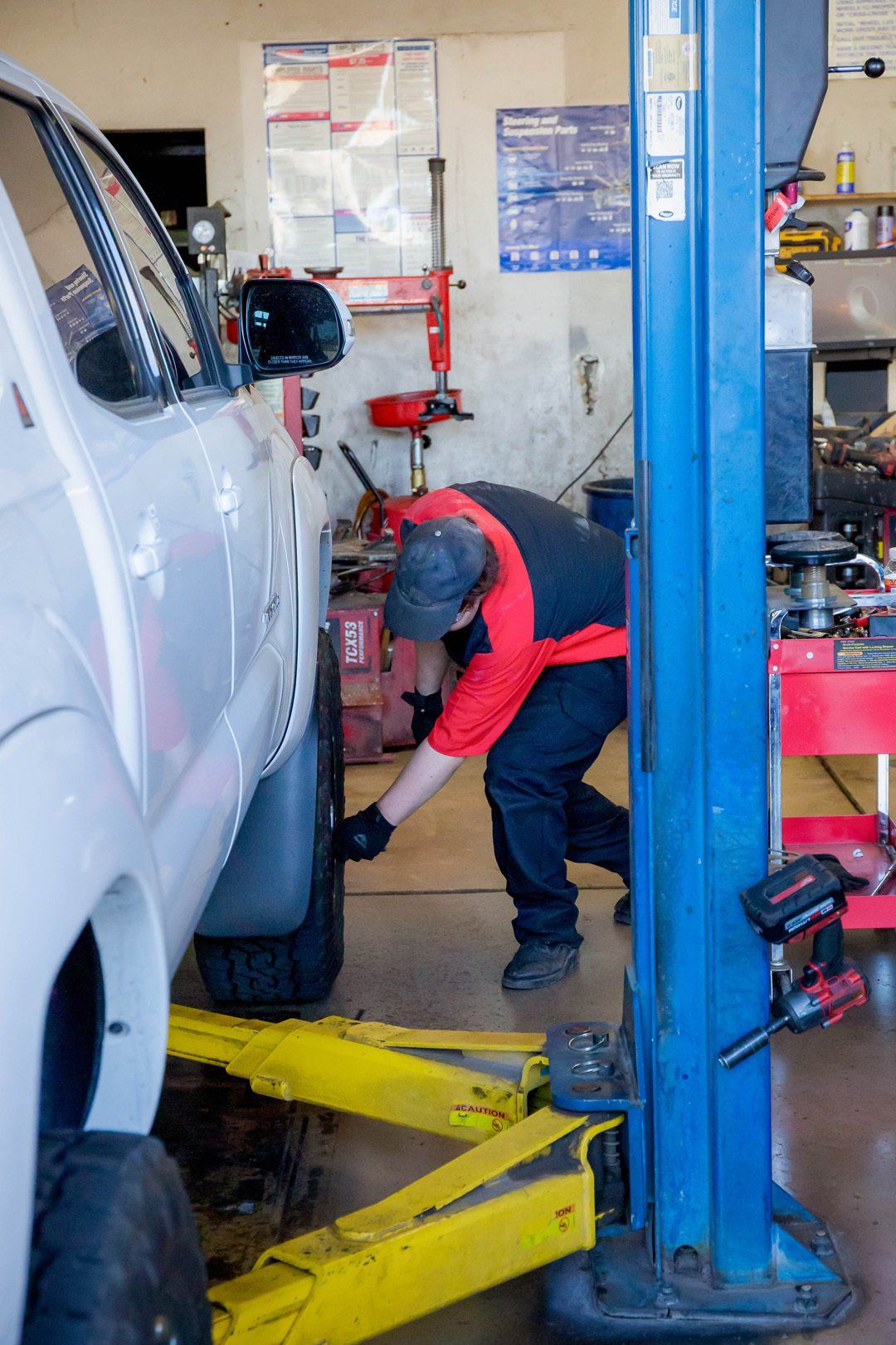 Mechanic working under a silver truck on a lift in an auto repair shop