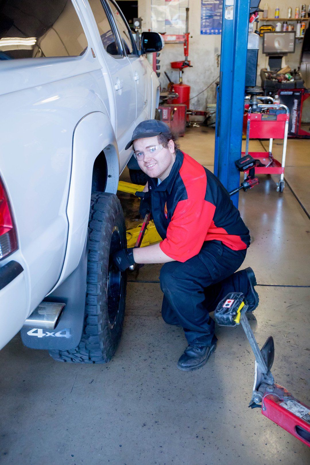 Mechanic kneeling beside white truck in a garage, working on the front wheel area.