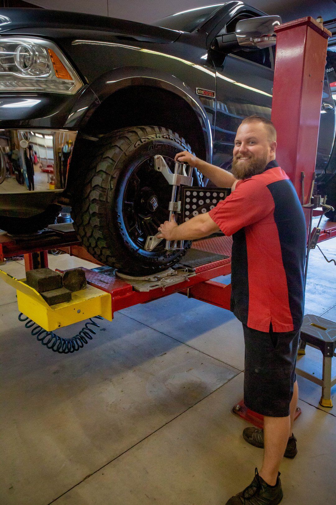 Mechanic measuring a lifted black truck’s tire in a repair shop