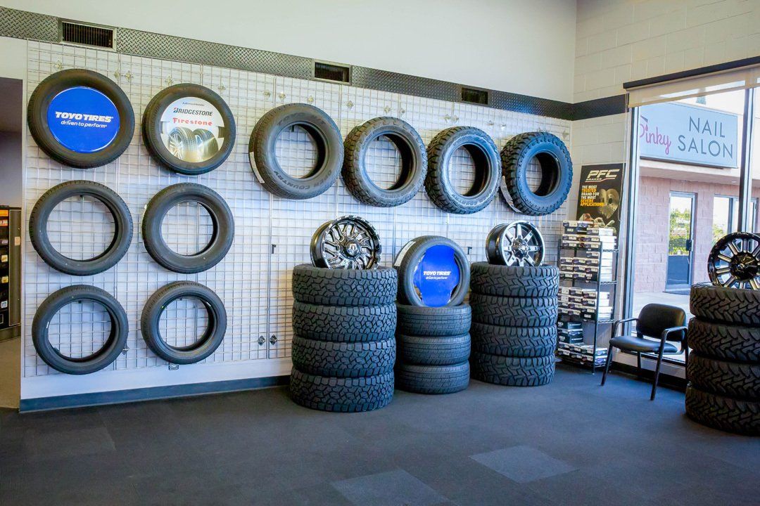 Tire shop interior with stacked tires, wall-mounted tires, and a blue “Nail Salon” sign in the background