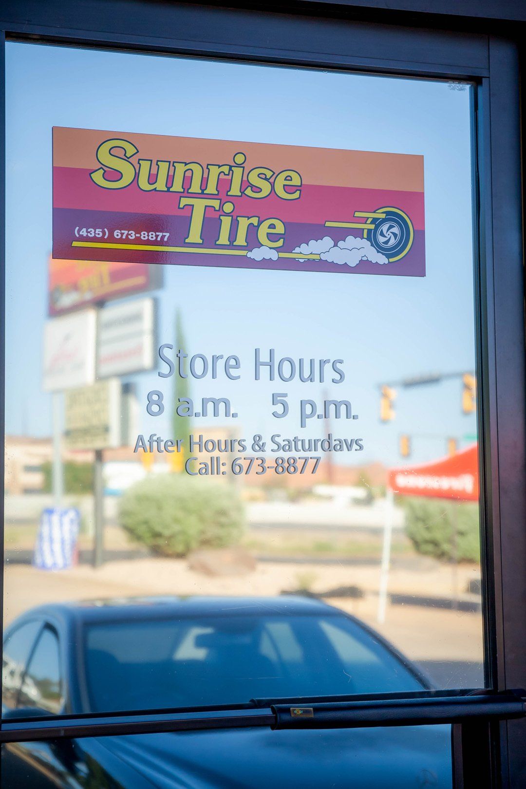 Sunrise Tire store window with hours sign and reflection of parked cars