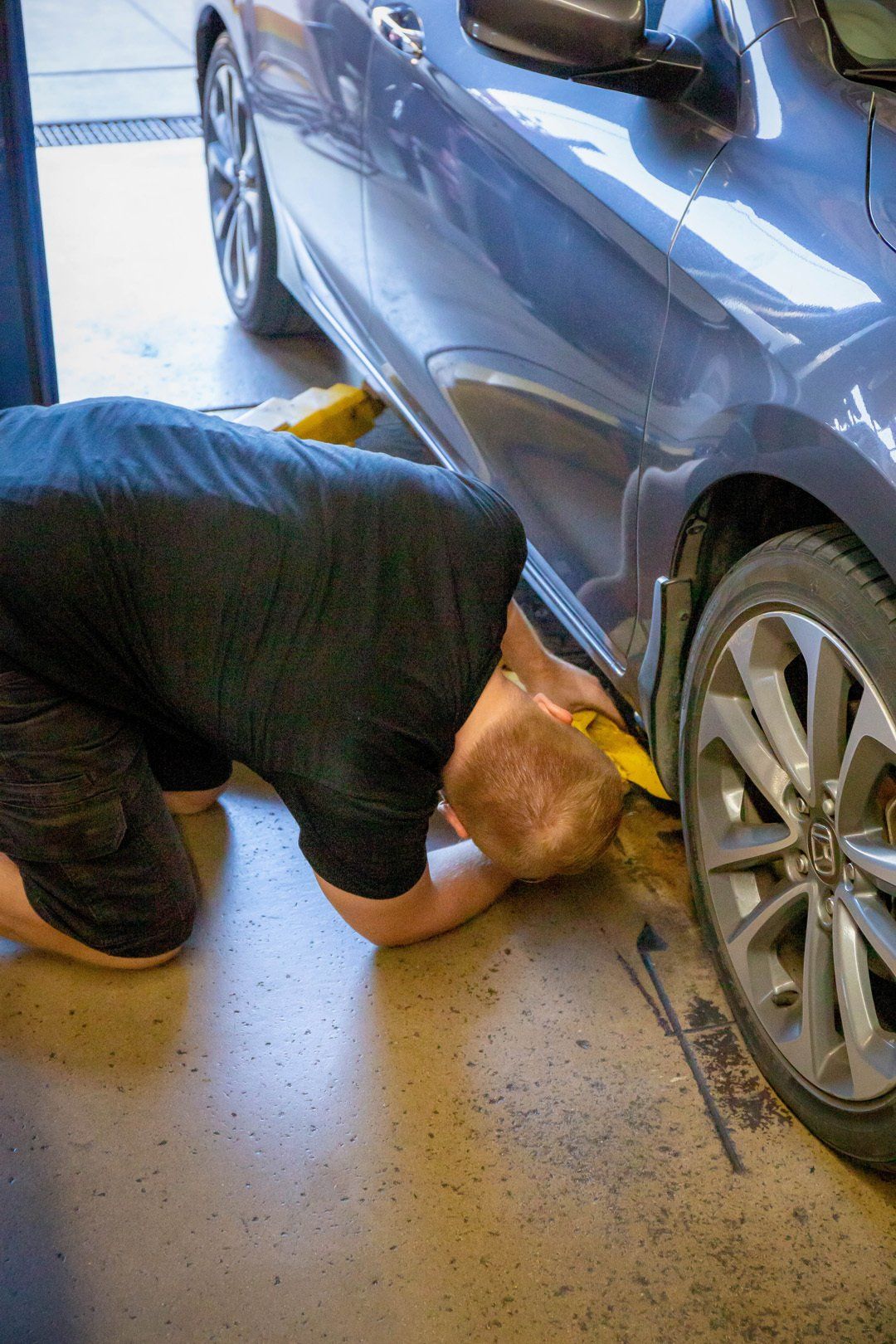 Mechanic working under a blue car near the front wheel in a garage