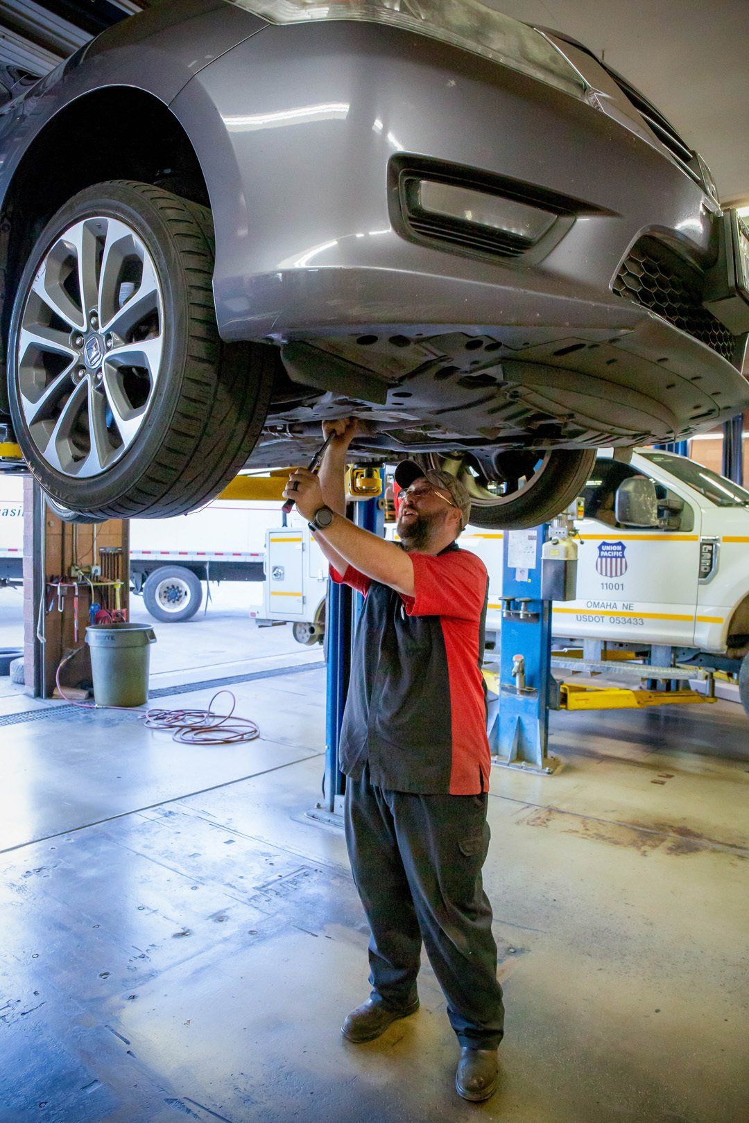 Mechanic inspecting the underside of a silver car on a lift in an auto repair shop