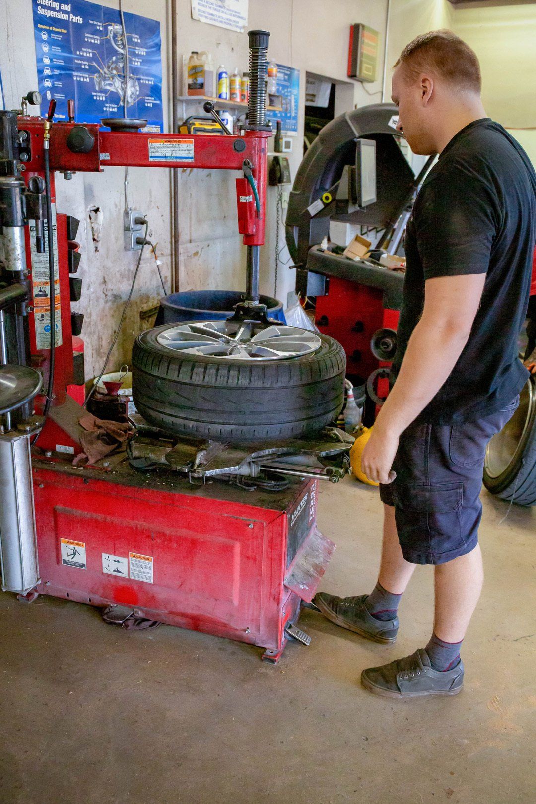 Mechanic standing by a red tire-changing machine with a car tire in a garage