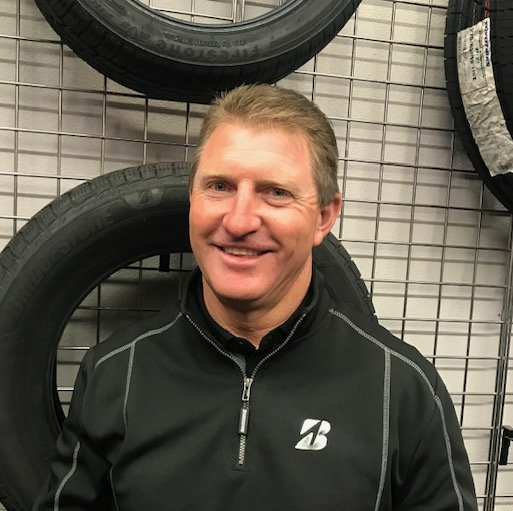 Smiling person in a black jacket standing before a wall of tires