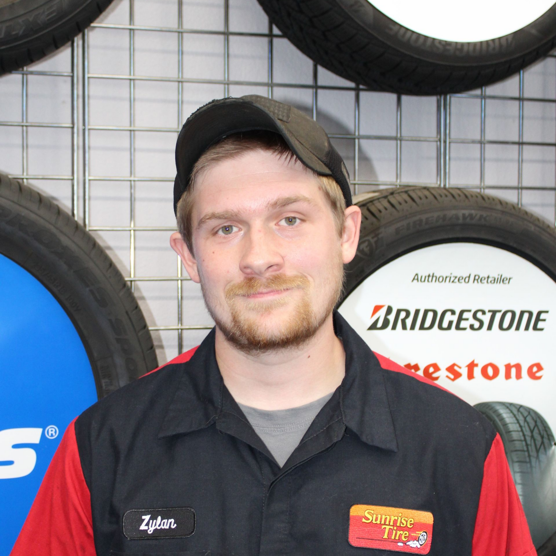 Man in black work shirt and cap standing in front of stacked tires and a Bridgestone display.