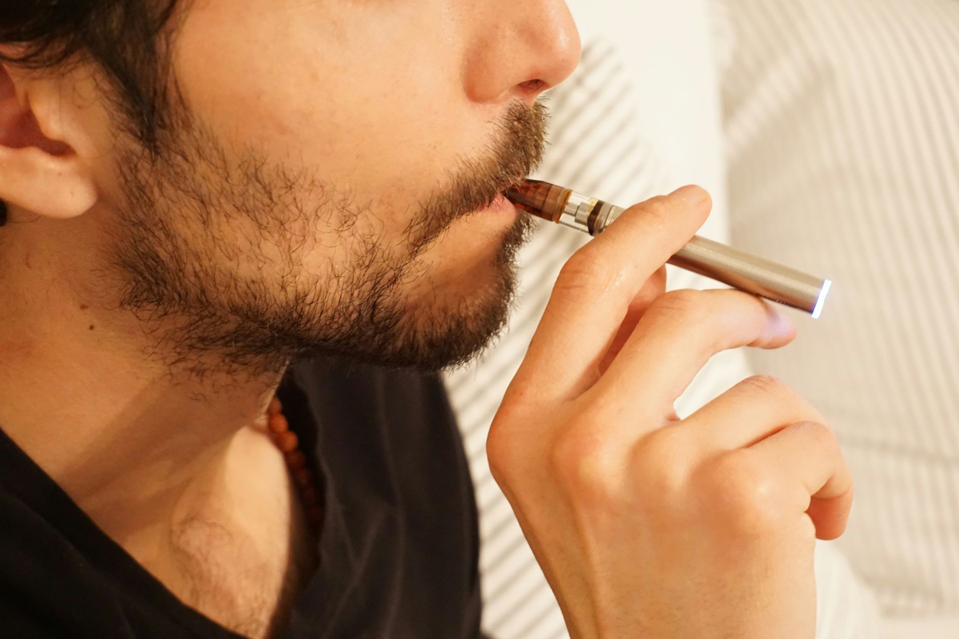 Man with beard vaping, holding vape to his mouth.