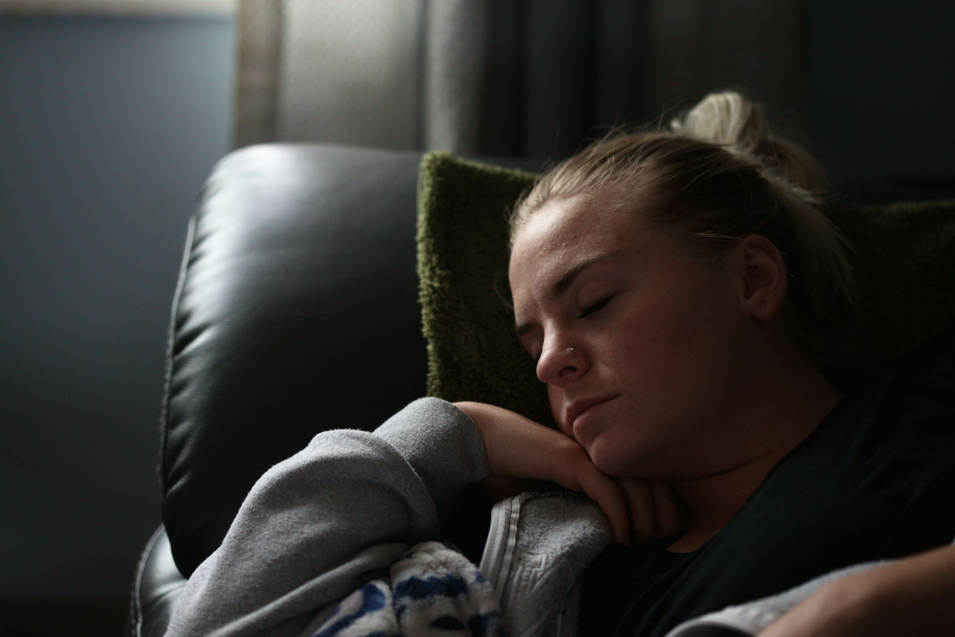 Woman asleep on a black leather chair, resting head on arm.