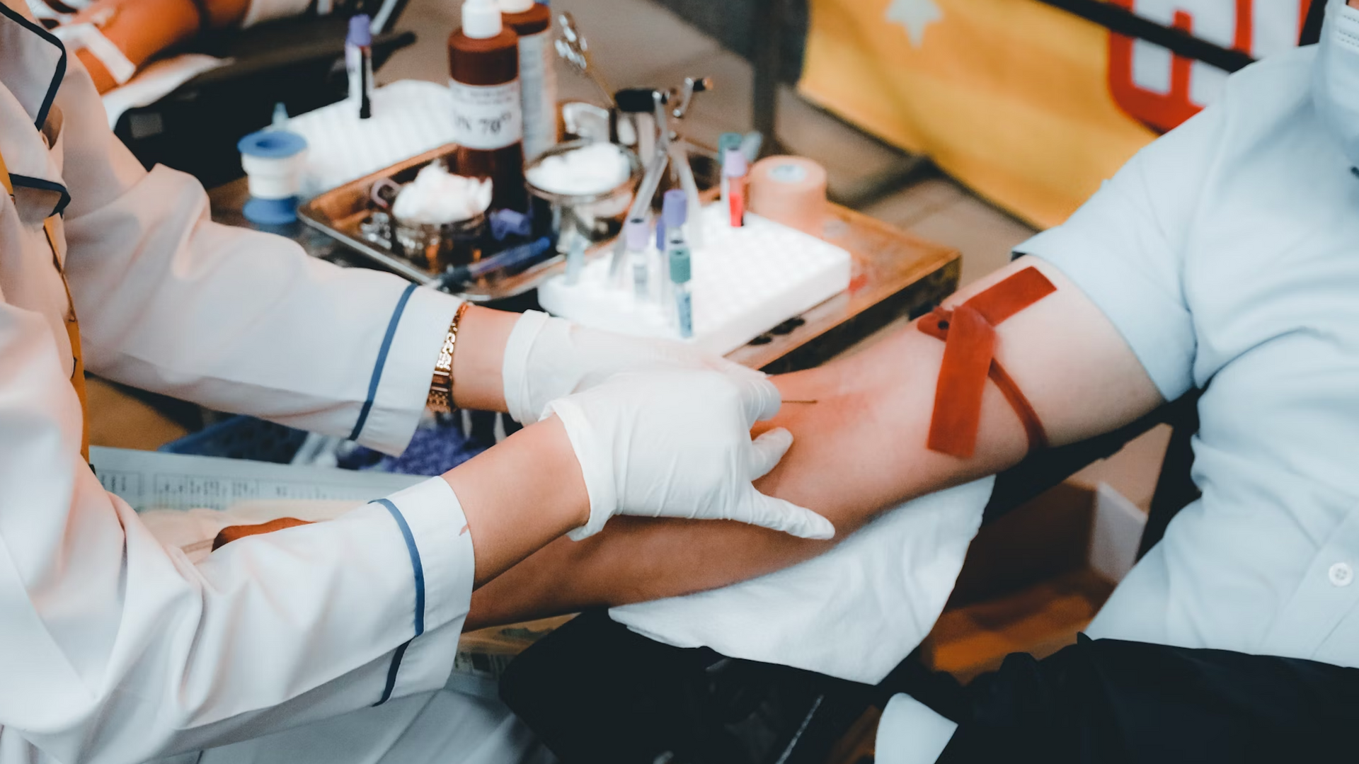 Person's arm with tourniquet, being prepared for blood draw. Medical professional in gloves, supplies in background.