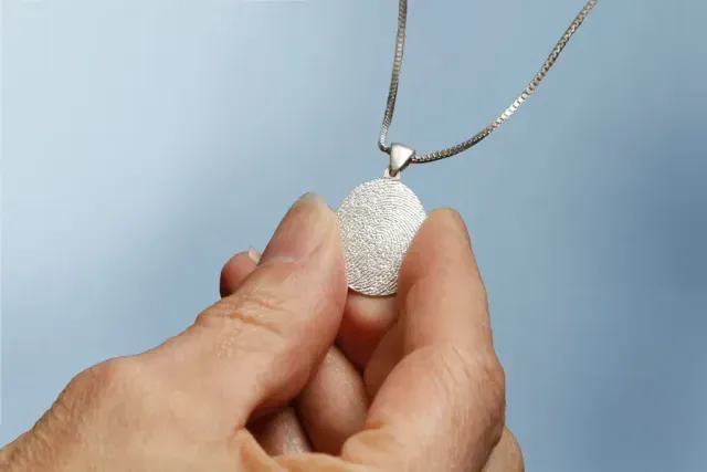 Hands holding a white pendant necklace with a silver chain against a light blue background