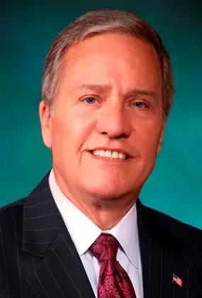 Portrait of a man in a dark suit and red tie against a teal studio background.