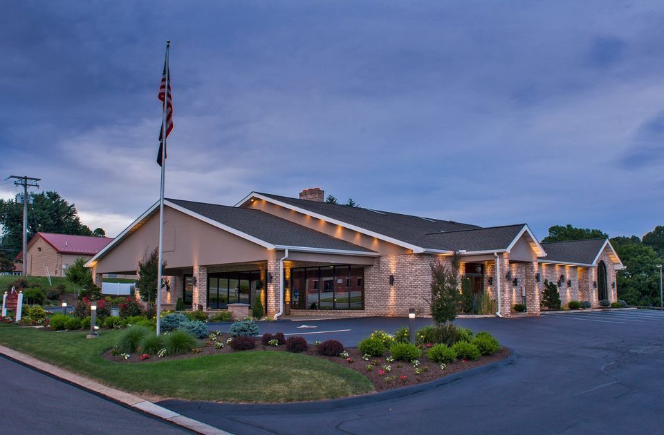 Single-story stone building with a flagpole and landscaped front entrance at dusk
