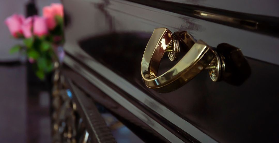 Close-up of a polished black coffin handle with a blurred floral arrangement in the background