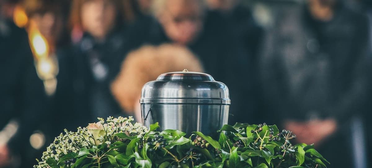 Silver urn on a bed of greenery, with a blurred crowd in the background