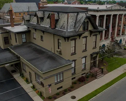 Historic beige building with gray roof and dormers beside a sidewalk and street, viewed from above