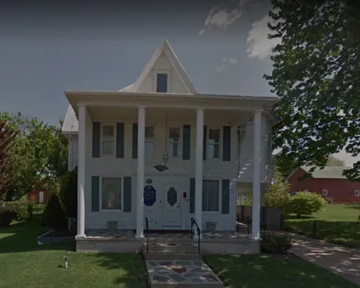 White two-story house with a front porch, blue shutters, and a walkway leading to the entrance.